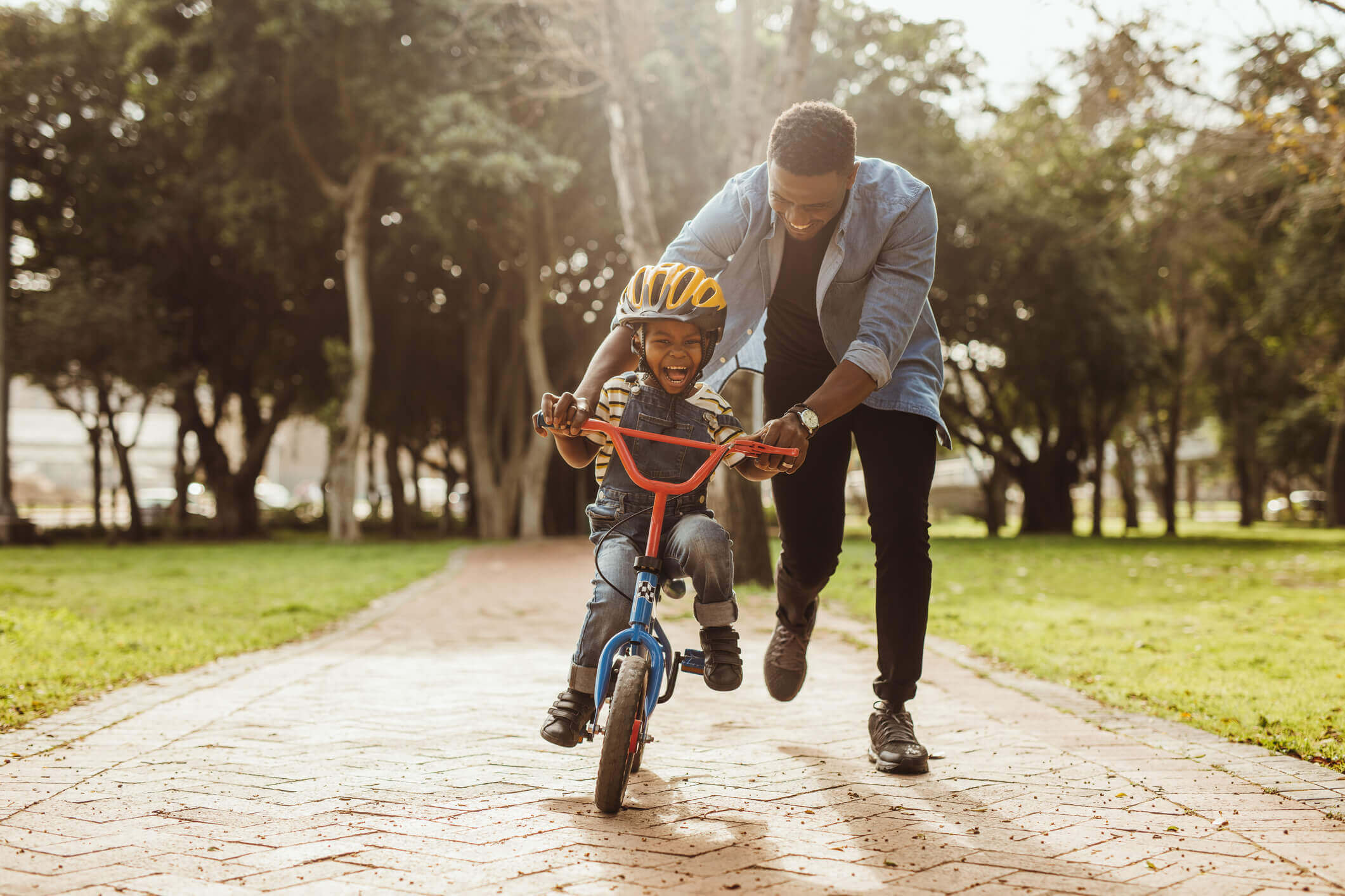 Man is pushing his son on a bike, teaching him to ride without training wheels.